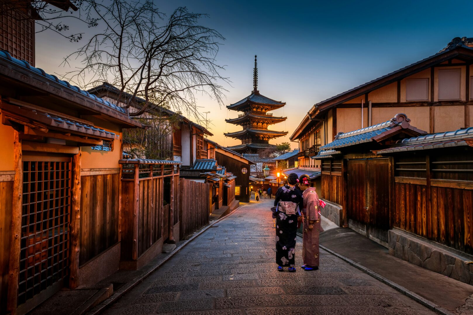 two women in traditional dress stand on the streeets of Kyoto at sunset