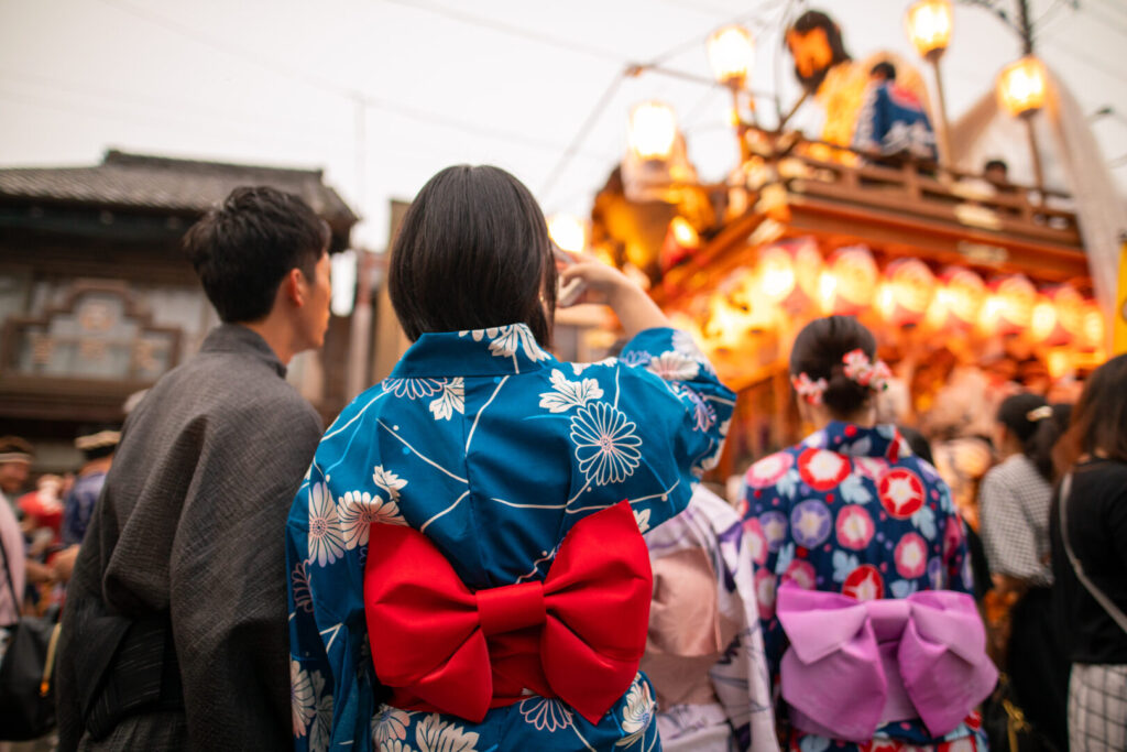 Young couple in yukata taking photos of matsuri parade, Japan seasons.