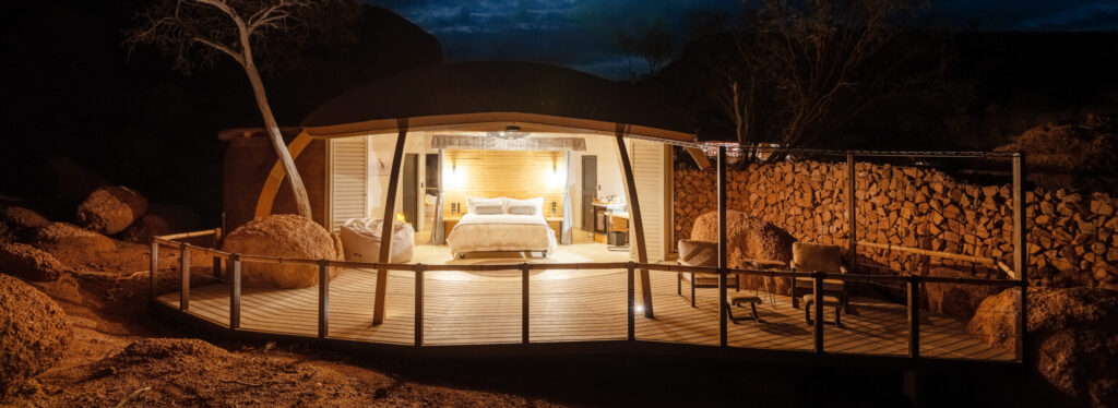 An illuminated suite interior seen from a deck at night, under a starlit sky.