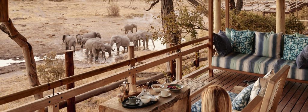 A guest on the deck at Savute Elephant Lodge watches elephants gathering at a waterhole in Chobe National Park.