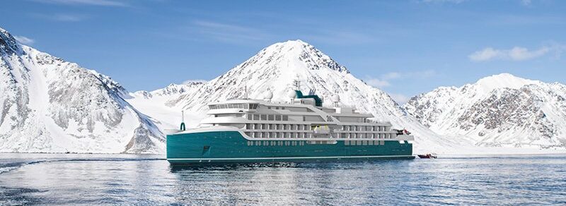 The expedition ship Sh Vega sits on calm water, reflected below, with snow covered peaks and glacial ice in the background.