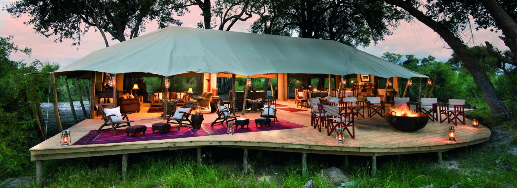 Duba Explorers Camp's canvas lounge and dining area beneath trees in the Okavango Delta.