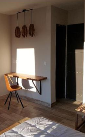 Minimalist lodge bedroom with a wooden wall-mounted desk, tan leather chair and woven pendant lights, lit by evening sun, Mantadia Lodge.
