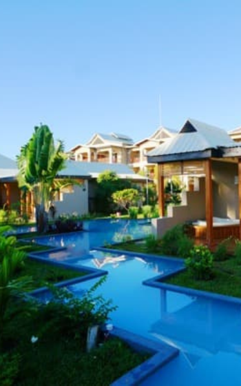 Winding blue swimming pool surrounded by tropical gardens and low-rise villas under a clear blue sky, Manjarano lodge.